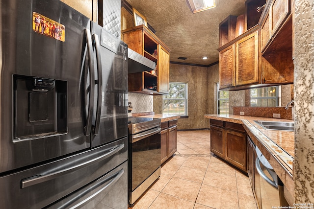 kitchen with wall chimney range hood, light tile patterned floors, a textured ceiling, sink, and stainless steel appliances