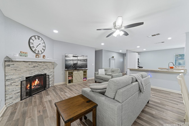 living room featuring a fireplace, sink, light wood-type flooring, and ceiling fan