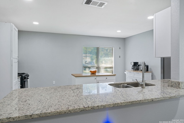 kitchen featuring kitchen peninsula, white cabinets, sink, light stone counters, and black gas range oven