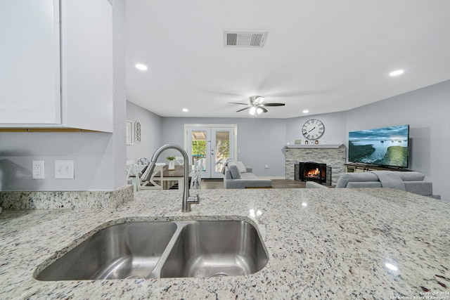 kitchen featuring sink, white cabinets, light stone counters, a fireplace, and ceiling fan