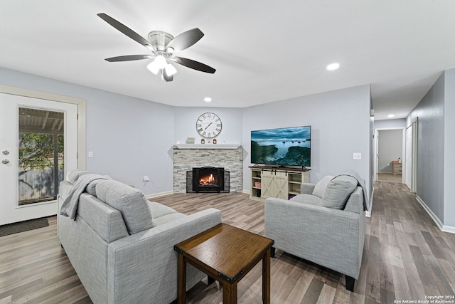 living room featuring a stone fireplace, wood-type flooring, and ceiling fan