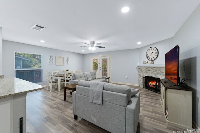 living room with french doors, ceiling fan, a stone fireplace, and hardwood / wood-style floors