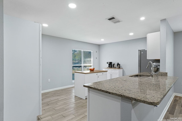 kitchen with light stone countertops, sink, kitchen peninsula, white cabinets, and light hardwood / wood-style flooring