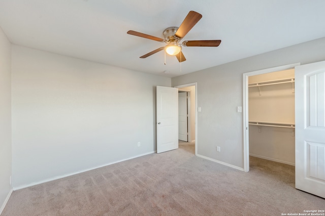 unfurnished bedroom with a walk in closet, a closet, light colored carpet, and ceiling fan