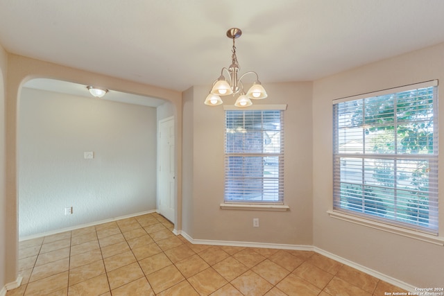 tiled spare room with a chandelier