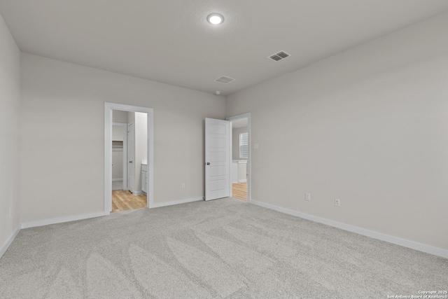 unfurnished bedroom featuring a spacious closet, connected bathroom, a closet, and light carpet