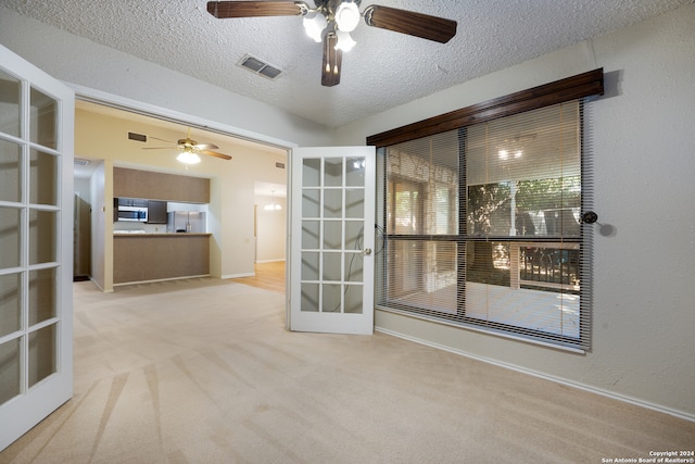 carpeted spare room with french doors, ceiling fan, and a textured ceiling