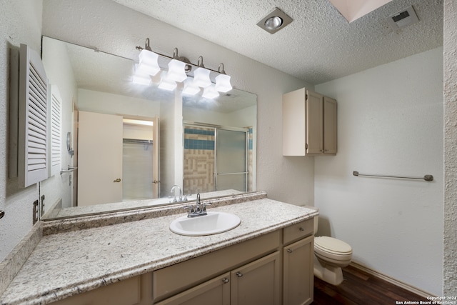 bathroom featuring a textured ceiling, hardwood / wood-style flooring, toilet, vanity, and an enclosed shower