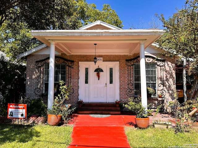 view of exterior entry with covered porch and a lawn