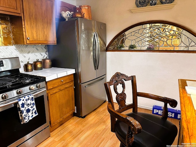 kitchen featuring tile countertops, light hardwood / wood-style flooring, stainless steel appliances, and backsplash