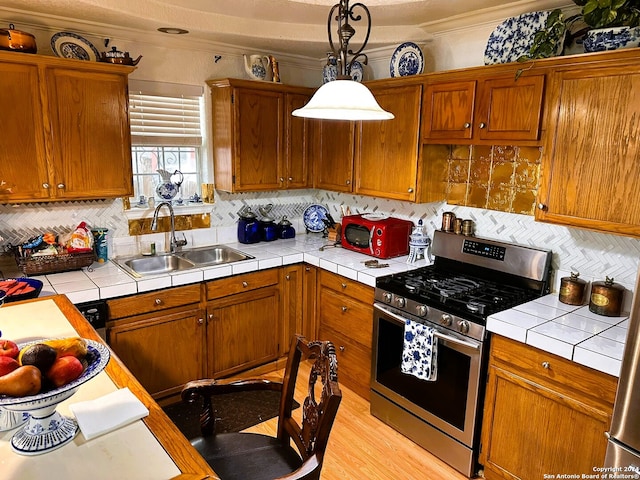 kitchen featuring hanging light fixtures, light hardwood / wood-style flooring, stainless steel range with gas stovetop, tile counters, and sink