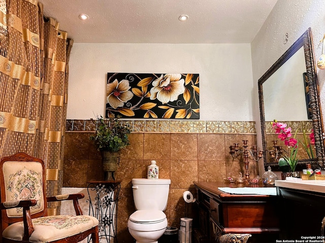 bathroom with toilet, a textured ceiling, vanity, and tile walls