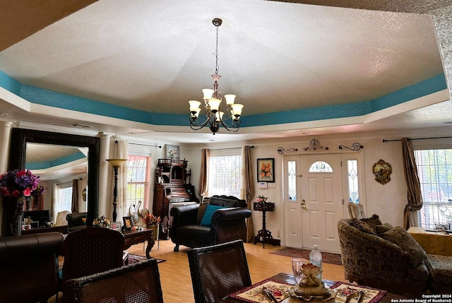 living room featuring a raised ceiling, decorative columns, a textured ceiling, light hardwood / wood-style floors, and a chandelier