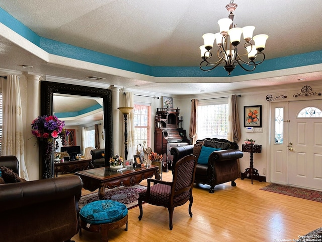 living room featuring ornamental molding, a raised ceiling, a chandelier, a textured ceiling, and light hardwood / wood-style floors