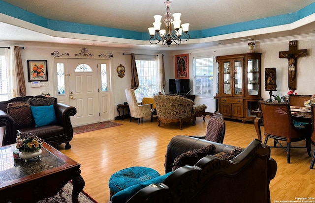 living room with light hardwood / wood-style floors, ornamental molding, a tray ceiling, and an inviting chandelier