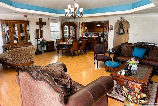 living room featuring ornamental molding, light hardwood / wood-style flooring, a notable chandelier, and a tray ceiling