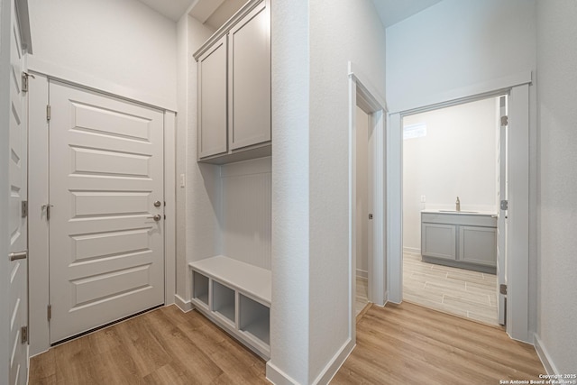mudroom with light wood-type flooring, baseboards, and a sink