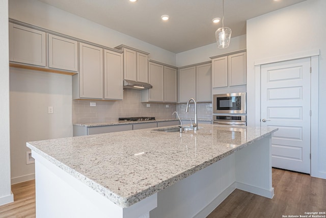 kitchen with stainless steel appliances, a sink, wood finished floors, and gray cabinets