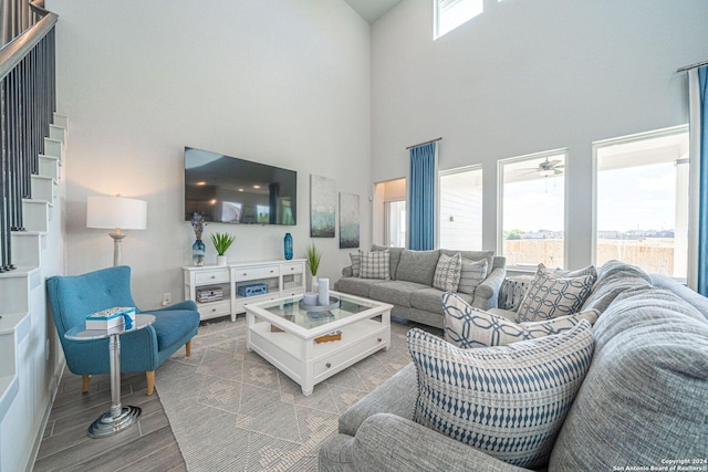 living area featuring a towering ceiling, ceiling fan, a wealth of natural light, and wood finished floors