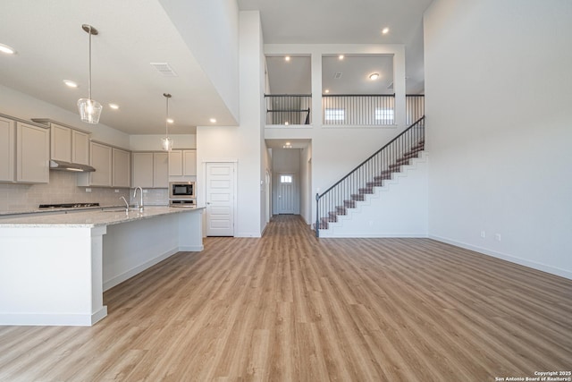 kitchen with stainless steel gas stovetop, under cabinet range hood, light wood-type flooring, gray cabinetry, and built in microwave