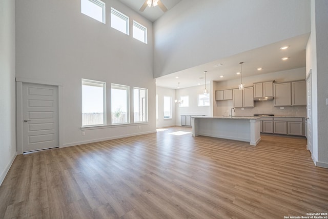 unfurnished living room featuring a sink, a ceiling fan, light wood finished floors, and a high ceiling