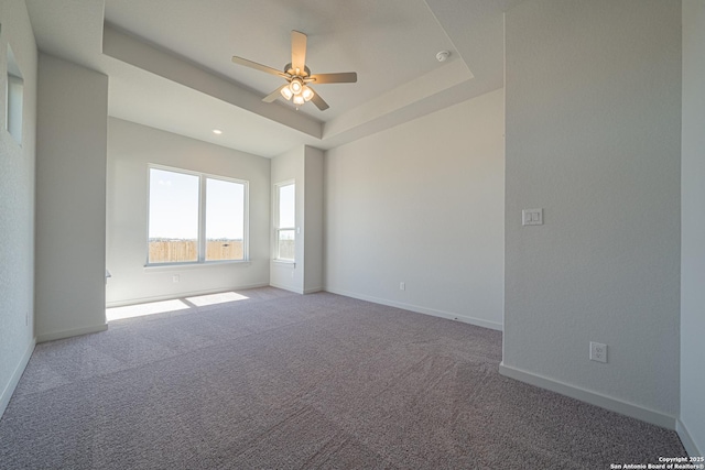 spare room featuring a tray ceiling, ceiling fan, carpet floors, and baseboards