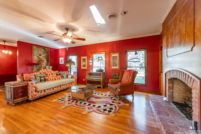 living room with ceiling fan, hardwood / wood-style flooring, a fireplace, a skylight, and crown molding