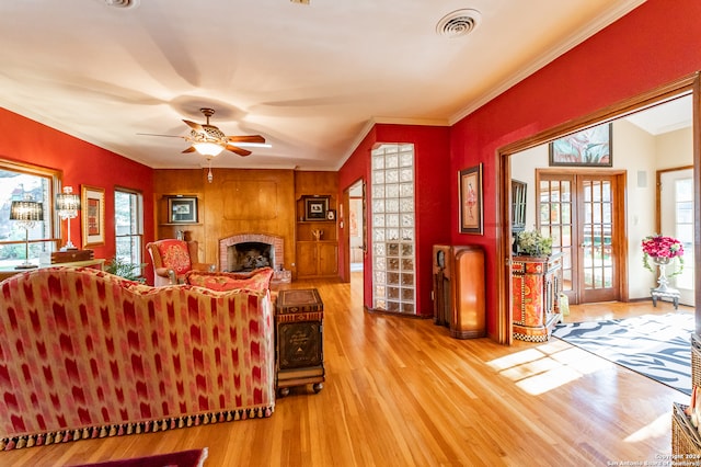 living room featuring ceiling fan, light hardwood / wood-style flooring, ornamental molding, a fireplace, and french doors