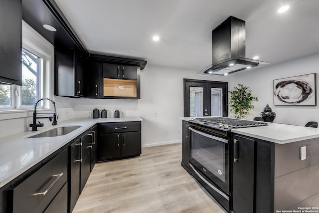 kitchen featuring sink, island exhaust hood, gas range, french doors, and light wood-type flooring