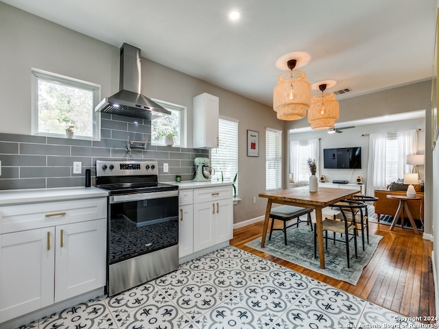 kitchen with wall chimney exhaust hood, electric range, decorative light fixtures, and white cabinetry