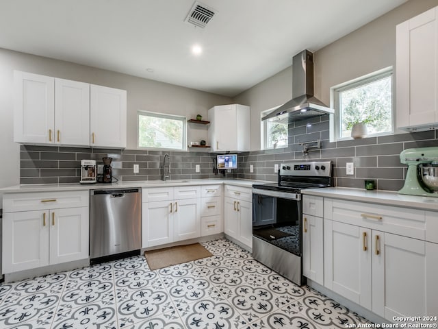 kitchen featuring white cabinetry, wall chimney exhaust hood, appliances with stainless steel finishes, and a wealth of natural light