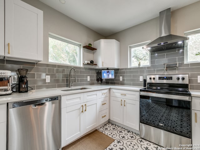 kitchen featuring appliances with stainless steel finishes, white cabinetry, and wall chimney range hood