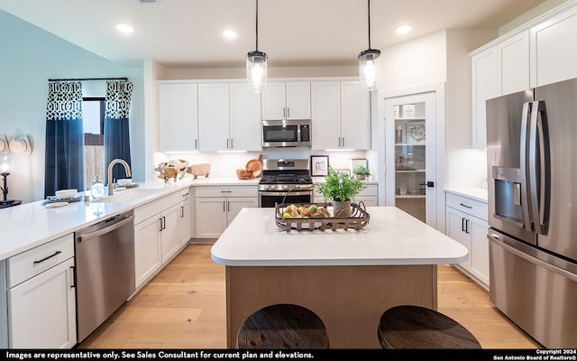 kitchen featuring light hardwood / wood-style flooring, stainless steel appliances, sink, pendant lighting, and white cabinetry