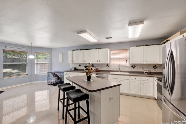 kitchen with appliances with stainless steel finishes, sink, white cabinetry, decorative light fixtures, and a breakfast bar