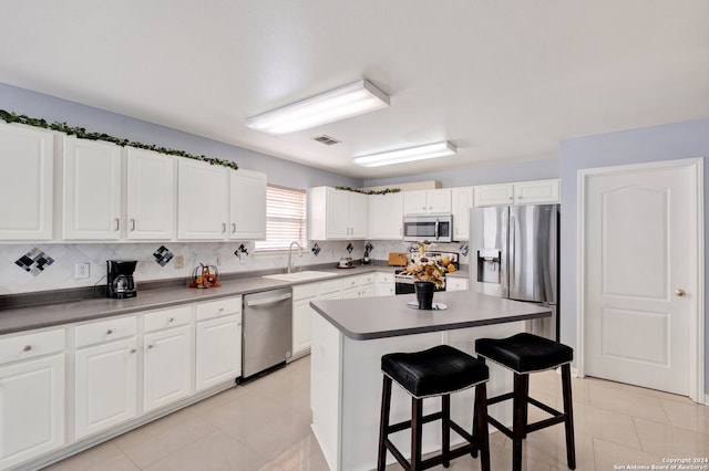 kitchen with appliances with stainless steel finishes, a breakfast bar, white cabinetry, sink, and a center island