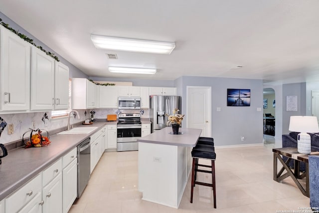 kitchen with a kitchen breakfast bar, white cabinetry, stainless steel appliances, sink, and a center island