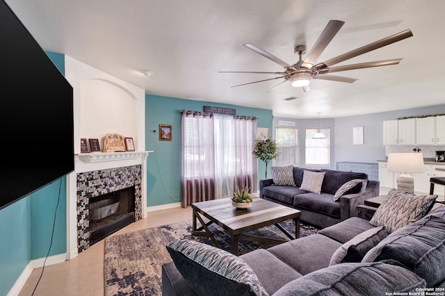 tiled living room featuring ceiling fan, a textured ceiling, and a fireplace