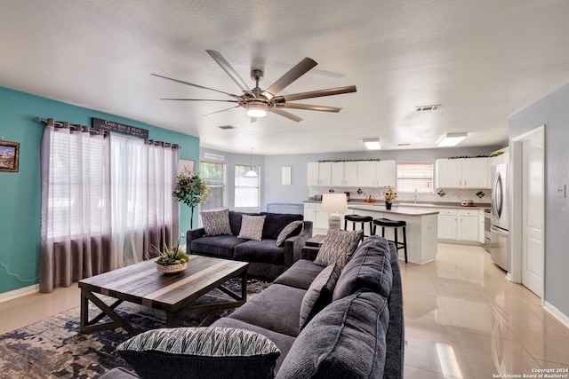 living room featuring ceiling fan, a textured ceiling, sink, and light tile patterned floors