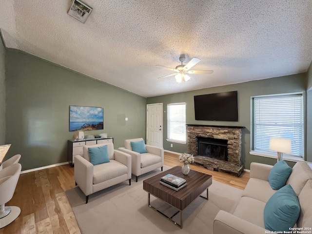 living room featuring lofted ceiling, ceiling fan, a textured ceiling, a stone fireplace, and light hardwood / wood-style floors