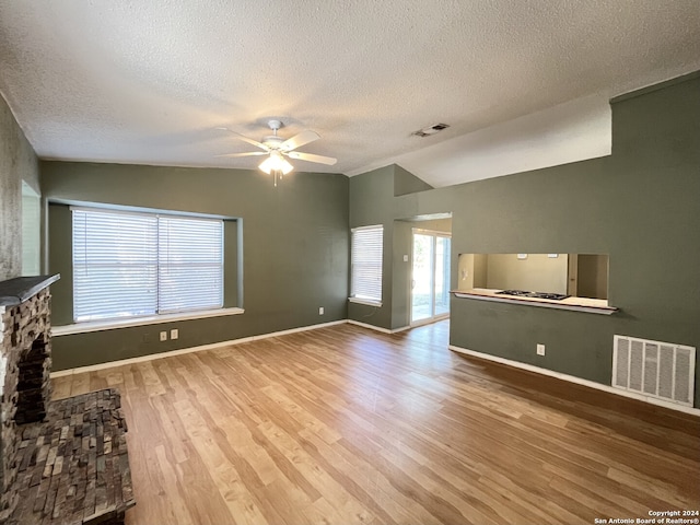 unfurnished living room with ceiling fan, a textured ceiling, hardwood / wood-style flooring, vaulted ceiling, and a stone fireplace