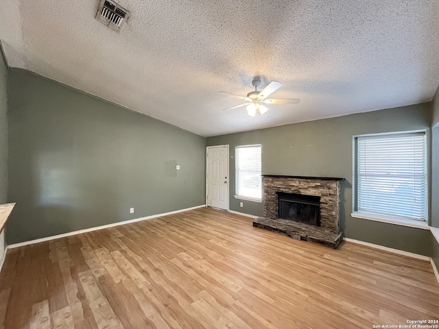 unfurnished living room featuring a stone fireplace, a textured ceiling, light wood-type flooring, and ceiling fan