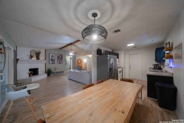 dining space with vaulted ceiling with beams, light hardwood / wood-style flooring, a textured ceiling, and a brick fireplace