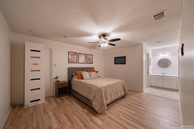 bedroom with light hardwood / wood-style floors, a textured ceiling, ensuite bath, and ceiling fan