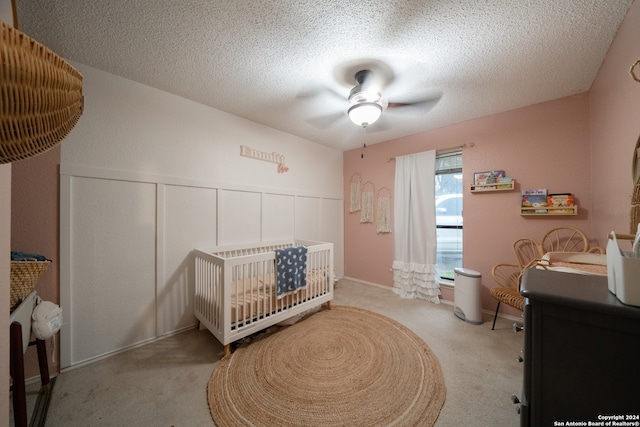 bedroom featuring light carpet, a nursery area, a textured ceiling, and ceiling fan