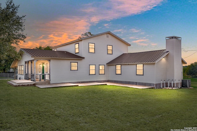 back house at dusk with a patio area and a lawn