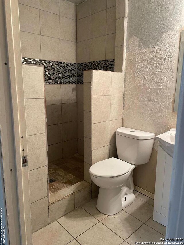 bathroom with toilet, tile patterned flooring, vanity, and tiled shower