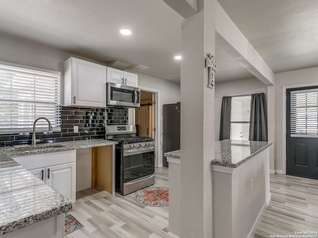 kitchen with white cabinetry, light wood-type flooring, stainless steel appliances, sink, and light stone counters