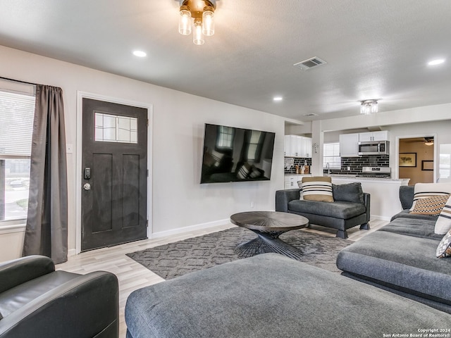 living room with ceiling fan, a textured ceiling, and light hardwood / wood-style flooring