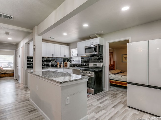 kitchen featuring light stone countertops, appliances with stainless steel finishes, white cabinetry, and light hardwood / wood-style floors