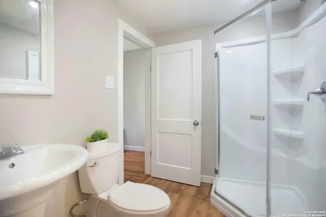 bathroom featuring toilet, sink, wood-type flooring, and a shower with door